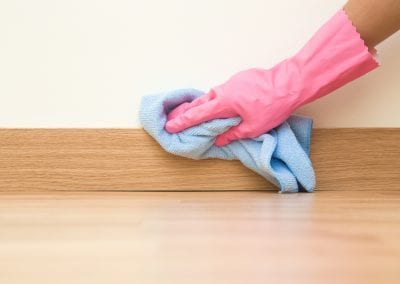 Cleaner with pink glove wiping a baseboard